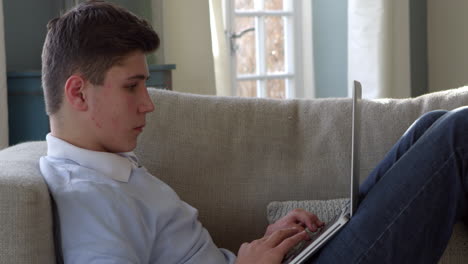 Teenage-Boy-Sitting-On-Sofa-Using-Laptop-At-Home-Shot-On-R3D