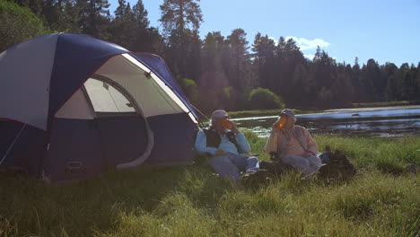 Down-panning-shot-of-senior-couple-outside-tent-near-lake
