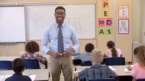 Happy-black-male-teacher-walking-through-class-toward-camera