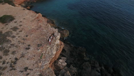 Aerial-Shot-Of-Friends-On-Cliffs-Watching-Sun-Set-Over-Sea