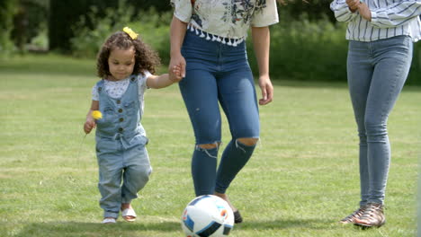 Mum-and-friends-kicking-a-ball-outdoors-with-young-daughter