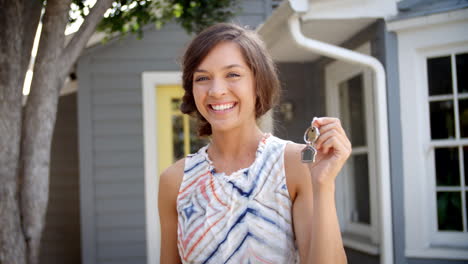 Portrait-Of-Happy-Woman-Standing-Outside-New-Home-With-Keys