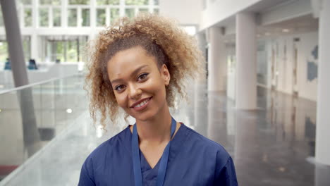 Portrait-Of-Smiling-Female-Nurse-In-Lobby-Of-Hospital