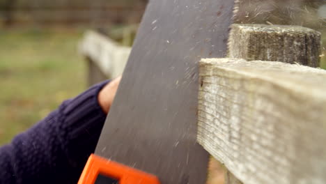 Close-Up-Of-Man-Fixing-Outdoor-Fence-With-Saw