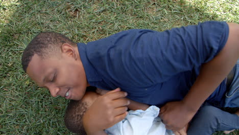 Mixed-race-black-father-play-fighting-with-young-son-in-park