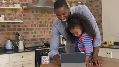 Father-And-Daughter-Using-Digital-Tablet-In-Kitchen-At-Home