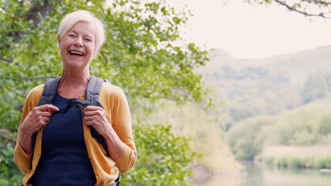 Slow-Motion-Portrait-Of-Laughing-Senior-Woman-Hiking-Along-Path-By-River-In-UK-Lake-District