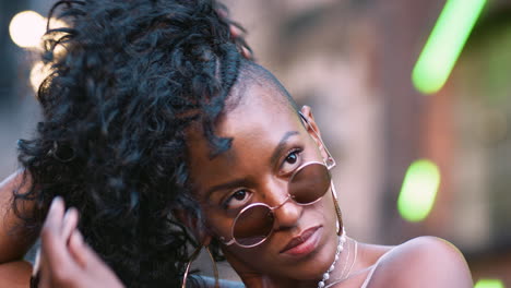 Fashionable-young-black-woman-playing-with-her-hair-and-laughing,close-up,-low-angle,-bokeh-lights-in-background