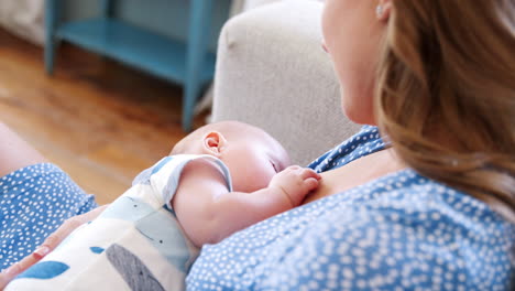 Over-The-Shoulder-Close-Up-Slow-Motion-Shot-Of-Mother-Sitting-On-Sofa-At-Home-And-Breastfeeding-Baby