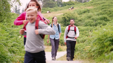 Children-running-ahead-of-parents-walking-on-a-countryside-path-during-a-family-camping-trip,-Lake-District,-UK