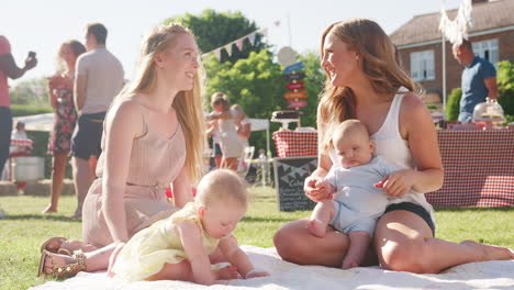 Zeitlupenaufnahme-Von-Zwei-Müttern,-Die-Auf-Einem-Teppich-Sitzen-Und-Mit-Babys-Beim-Sommergartenfest-Spielen