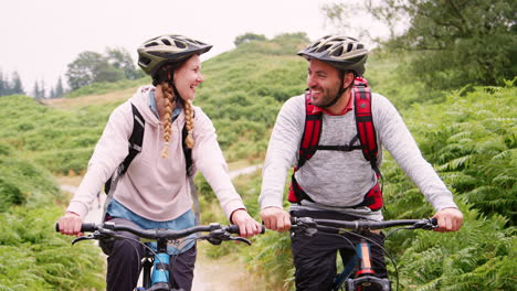 Young-adult-couple-sitting-on-mountain-bikes,-close-up,-Lake-District,-UK