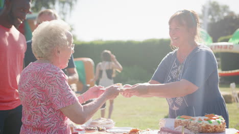 Slow-Motion-Shot-Of-Senior-Woman-Being-Served-At-Cake-Stall-At-Summer-Garden-Fete