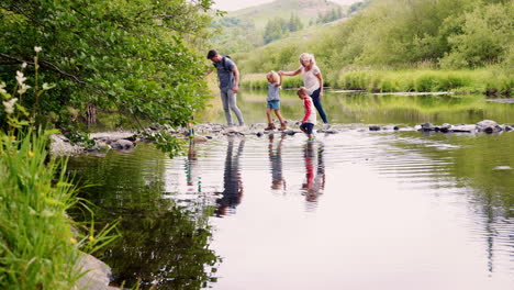 Zeitlupenaufnahme-Von-Eltern,-Die-Ihren-Kindern-Beim-Wandern-Im-Britischen-Seengebiet-Helfen,-Den-Fluss-Zu-überqueren
