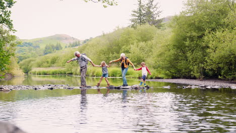 Slow-Motion-Shot-Of-Grandparents-Helping-Grandchildren-To-Cross-River-Whilst-Hiking-In-UK-Lake-District