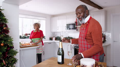 Senior-Schwarzer-Mann-Gießt-Champagner-Für-Seinen-Partner-In-Der-Küche,-Während-Sie-Am-Weihnachtstag-Das-Abendessen-Vorbereiten