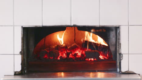 Close-up-of-wood-burning-in-the-clay-oven-at-an-artisan-bakery,-front-view