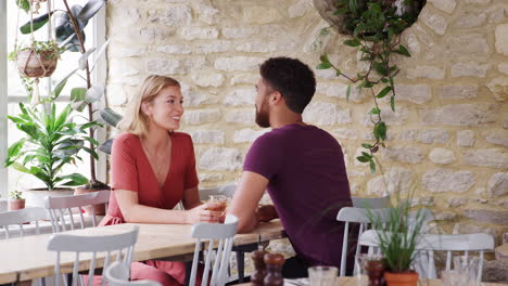 Mixed-race-young-adult-couple-sitting-at-table-talking-in-an-empty-restaurant