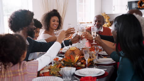 Multi-generation-mixed-race-family-raising-glasses-to-make-a-toast-sitting-at-their-Thanksgiving-dinner-table,-close-up
