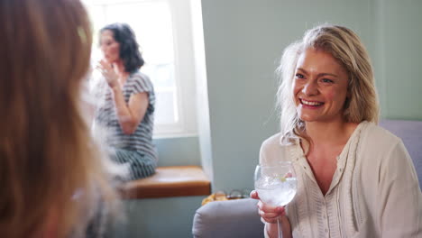 Young-adult-white-woman-holding-a-drink-and-talking-with-her-friend,-sitting-in-the-lounge-room-at-a-pub,-close-up,-over-shoulder-view