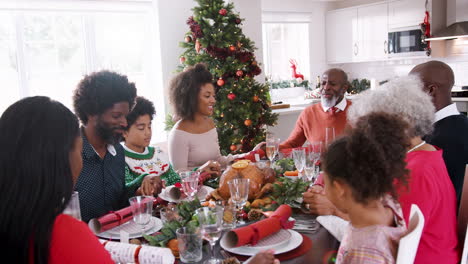 Multi-generation-mixed-race-family-sitting-at-Christmas-dinner-table-holding-hands-and-saying-grace,-selective-focus