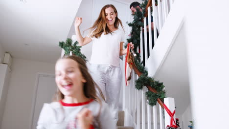 Aufgeregte-Familie-Im-Schlafanzug-Läuft-Am-Weihnachtsmorgen-Mit-Strümpfen-Die-Treppe-Hinunter
