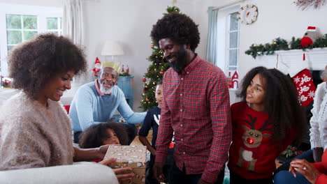 Couple-Exchanging-Gifts-As-Multi-Generation-Family-Celebrate-Christmas-At-Home-Together