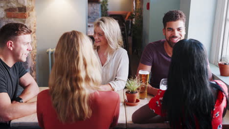 Mixed-race-group-of-young-adult-friends-sitting-at-a-table-in-a-pub-talking,-close-up