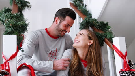 Portrait-Of-Excited-Couple-Wearing-Pajamas-Sitting-On-Stairs-On-Christmas-Morning