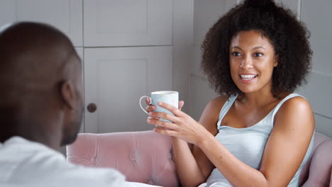 Young-mixed-race-couple-relax-together,-drinking-coffee-and-talking-in-their-living-room,-close-up,-over-shoulder-view