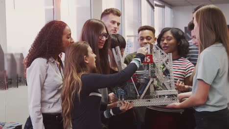 College-Students-With-Female-Teacher-Holding-Machine-In-Science-Or-Robotics-Class