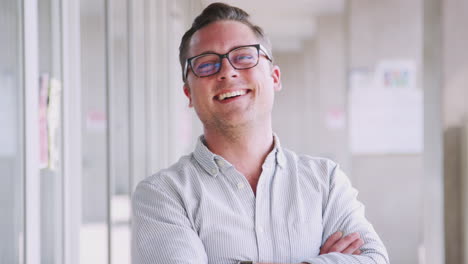 Portrait-Of-Smiling-Male-School-Teacher-Standing-In-Corridor-Of-College-Building