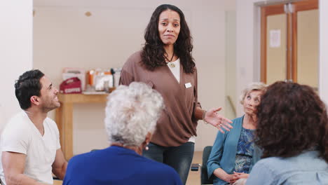 Mature-Woman-Standing-To-Address-Self-Help-Therapy-Group-Meeting-In-Community-Center