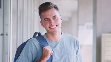 Portrait-Of-Smiling-Male-University-Student-With-Backpack-In-Corridor-Of-College-Building