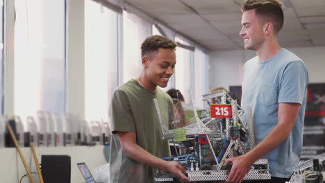 Two-Male-University-Students-Holding-Machine-In-Science-Robotics-Or-Engineering-Class