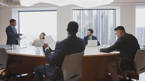 Reifer-Geschäftsmann-Hält-Im-Modernen-Büro-Eine-Präsentation-Vor-Kollegen,-Die-Am-Tisch-Sitzen