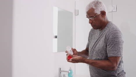 Senior-Man-In-Bathroom-Mirror-Wearing-Pajamas-Taking-Vitamin-Supplement-Tablets