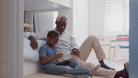Großvater-Sitzt-Mit-Enkel-Im-Kinderzimmer-Und-Nutzt-Gemeinsam-Ein-Digitales-Tablet