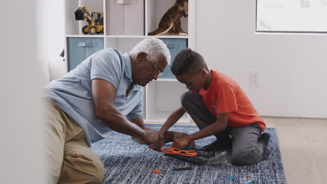Grandfather-With-Grandson-Sitting-On-Rug-At-Home-Building-Model-Helicopter-Together