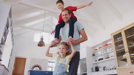 Daughter-Playing-Game-Walking-On-Fathers-Feet-With-Son-On-Shoulders-At-Home