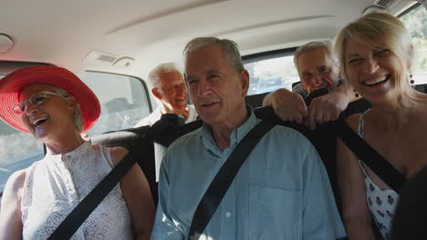 Group-Of-Senior-Friends-Sitting-In-Back-Of-People-Carrier-Being-Driven-To-Vacation