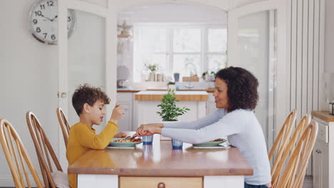 Single-Mother-Helping-Son-To-Cut-Food-As-They-Sit-At-Table-Eating-Meal-At-Home
