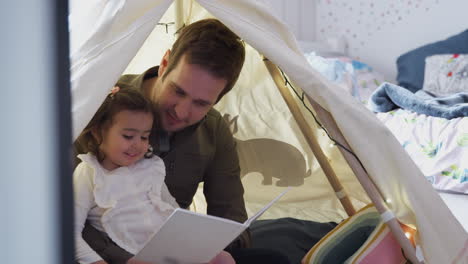 Single-Father-Reading-With-Daughter-In-Den-In-Bedroom-At-Home