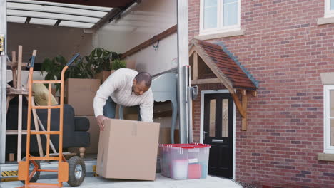 Man-Unloading-Boxes-From-Removal-Truck-Outside-New-Home-On-Moving-Day