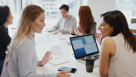 Team-Of-Young-Businesswomen-With-Laptop-Meeting-Around-Table-In-Modern-Workspace