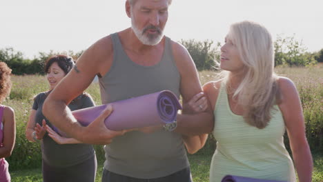 Gruppe-Reifer-Männer-Und-Frauen-Mit-Trainingsmatten-Am-Ende-Des-Outdoor-Yoga-Kurses