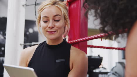 Female-Personal-Trainer-With-Female-Boxer-In-Gym-Checking-Performance-Using-Digital-Tablet
