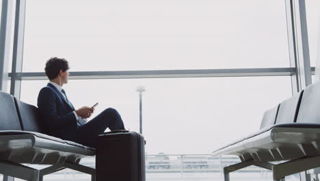 Businessman-Sitting-In-Airport-Departure-Lounge-Using-Mobile-Phone