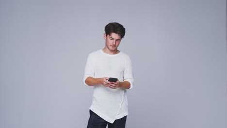 Studio-Shot-Of-Man-Against-White-Background-Sending-Text-Message-On-Mobile-Phone-In-Slow-Motion