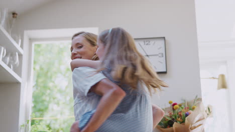 Mother-Giving-Smiling-Daughter-Piggyback-Ride-In-Kitchen-At-Home